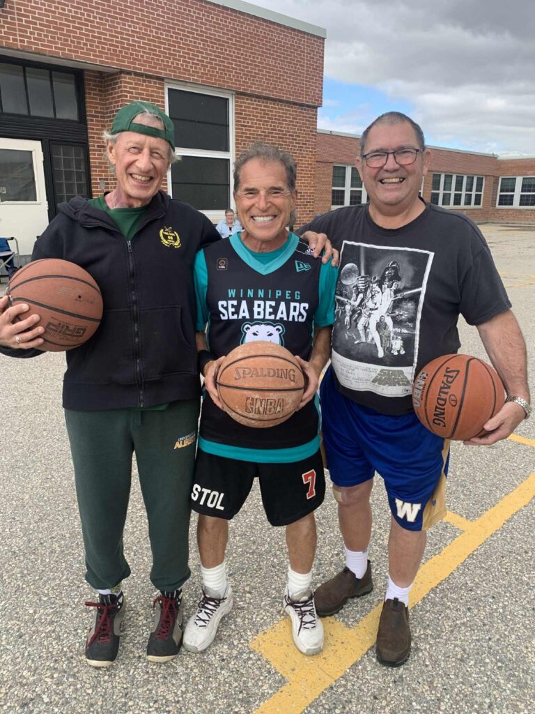 reconnecting: 3 men each holding a basketball on an asphalt court in front of a school