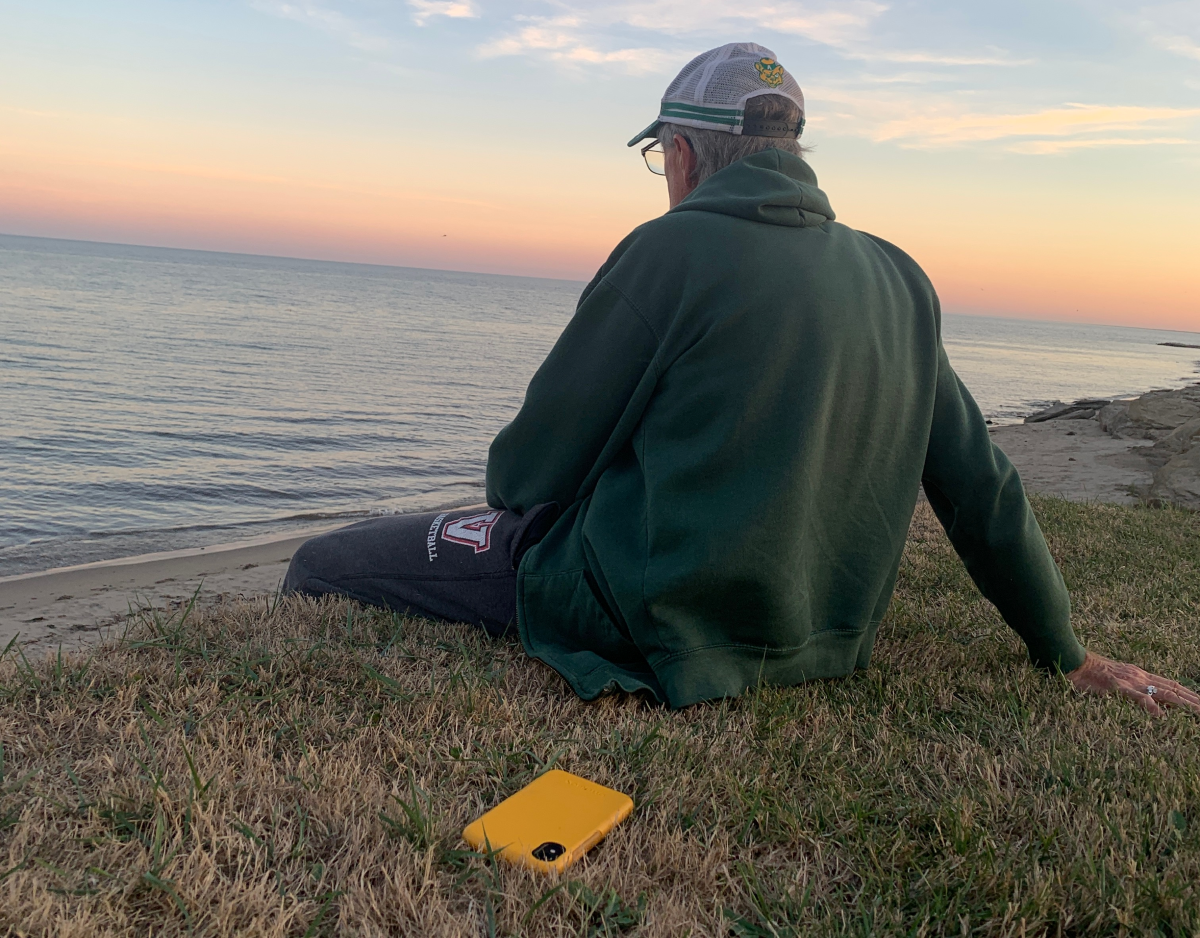 Happiness - a man sitting on a bluff overlooking the ocean, looking away from the camera, with his cellphone on the ground behind him